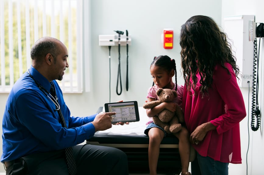 Healthcare worker talking with parent and child in exam room.