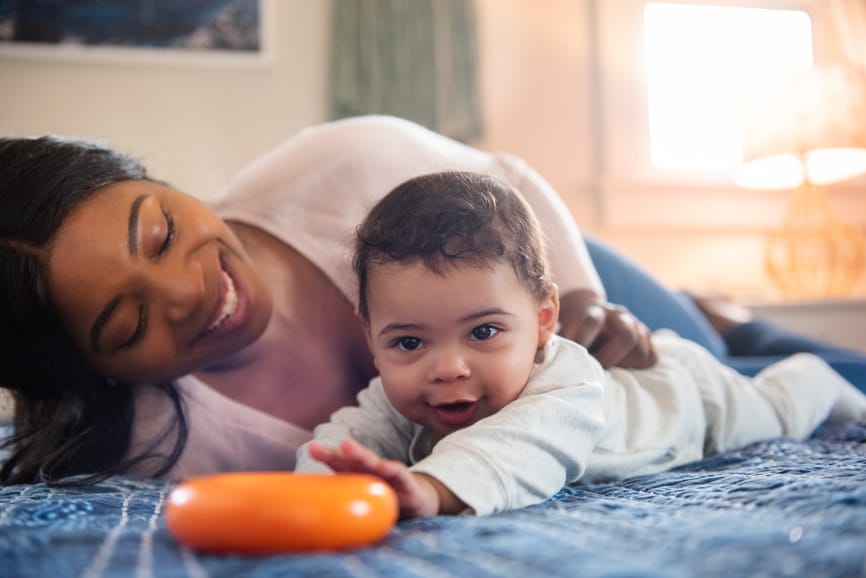 Mother and baby on bed, baby reaching for toy