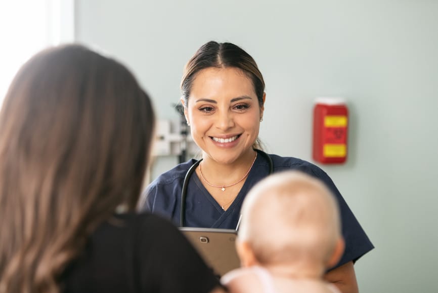 Doctor holds a digital tablet and talks while the mother holds her infant.