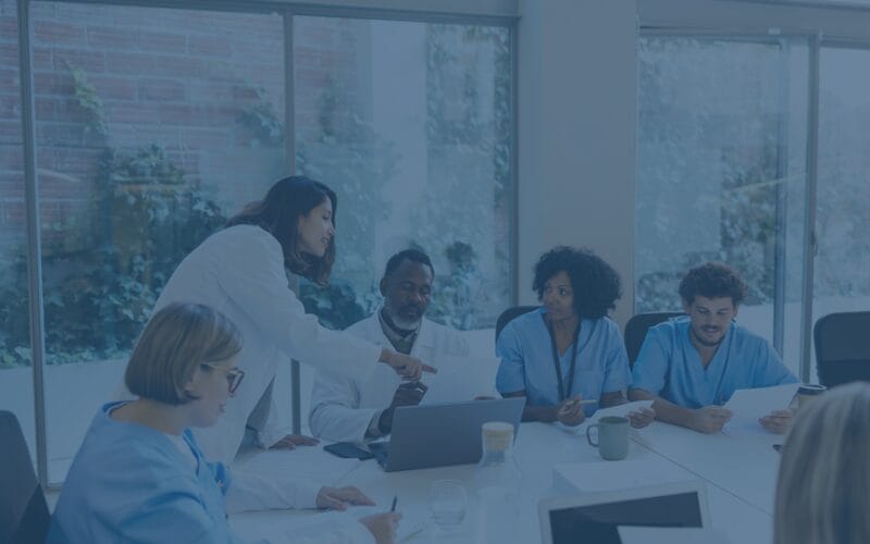 Several healthcare workers at a table with a leader talking to them,